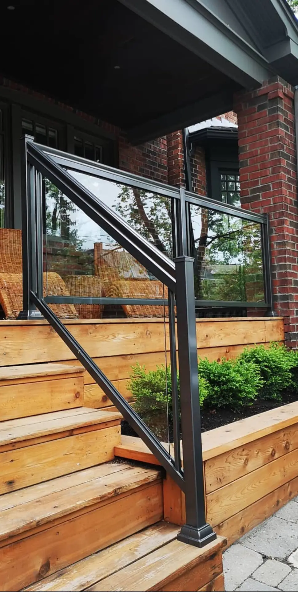 Black framed glass railings beside a timber deck and exterior stairs at a brick home