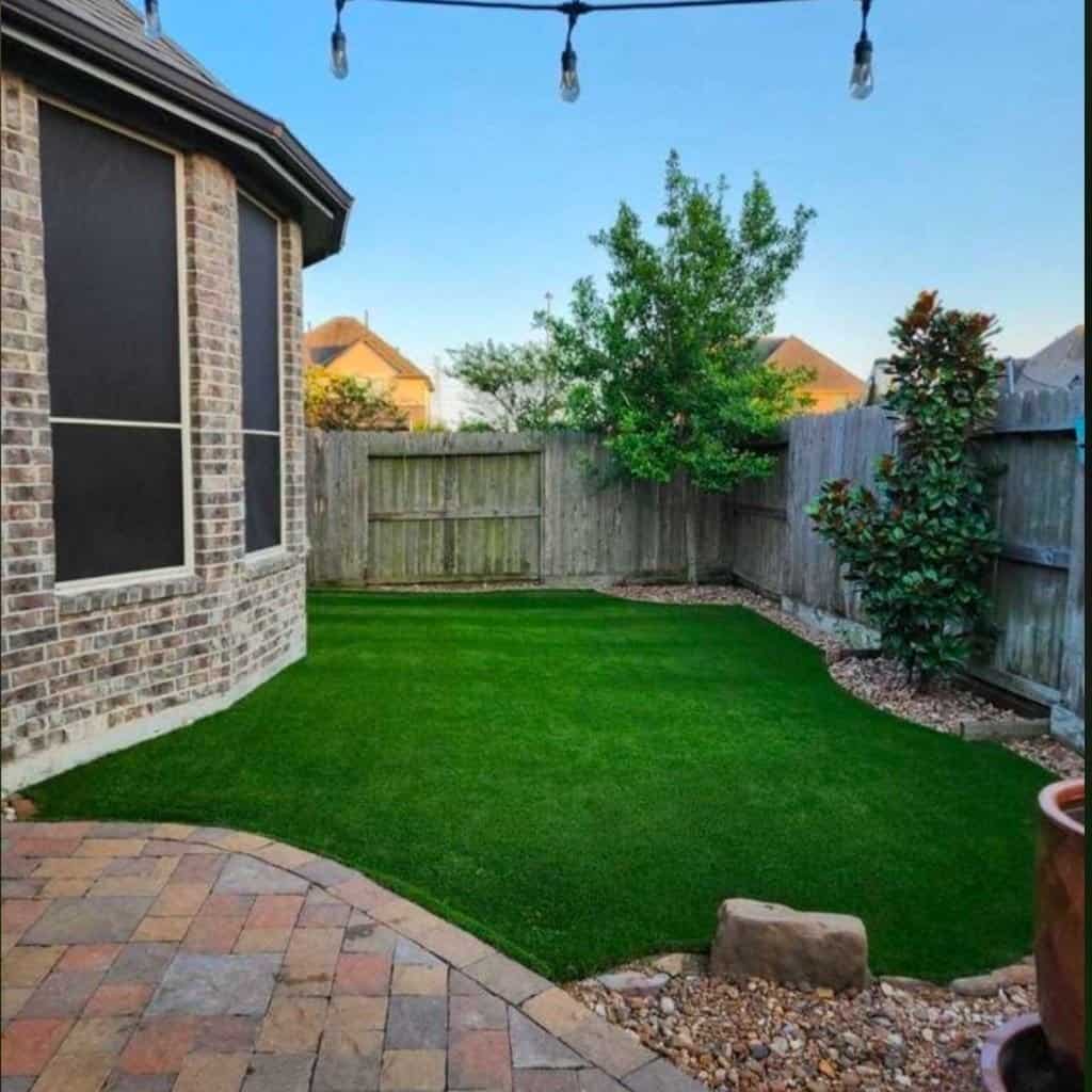 A backyard with a brick patio and artifical grass